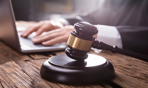 Close-up Of A Gavel On Wooden Desk In Front Of Judge Working On Laptop